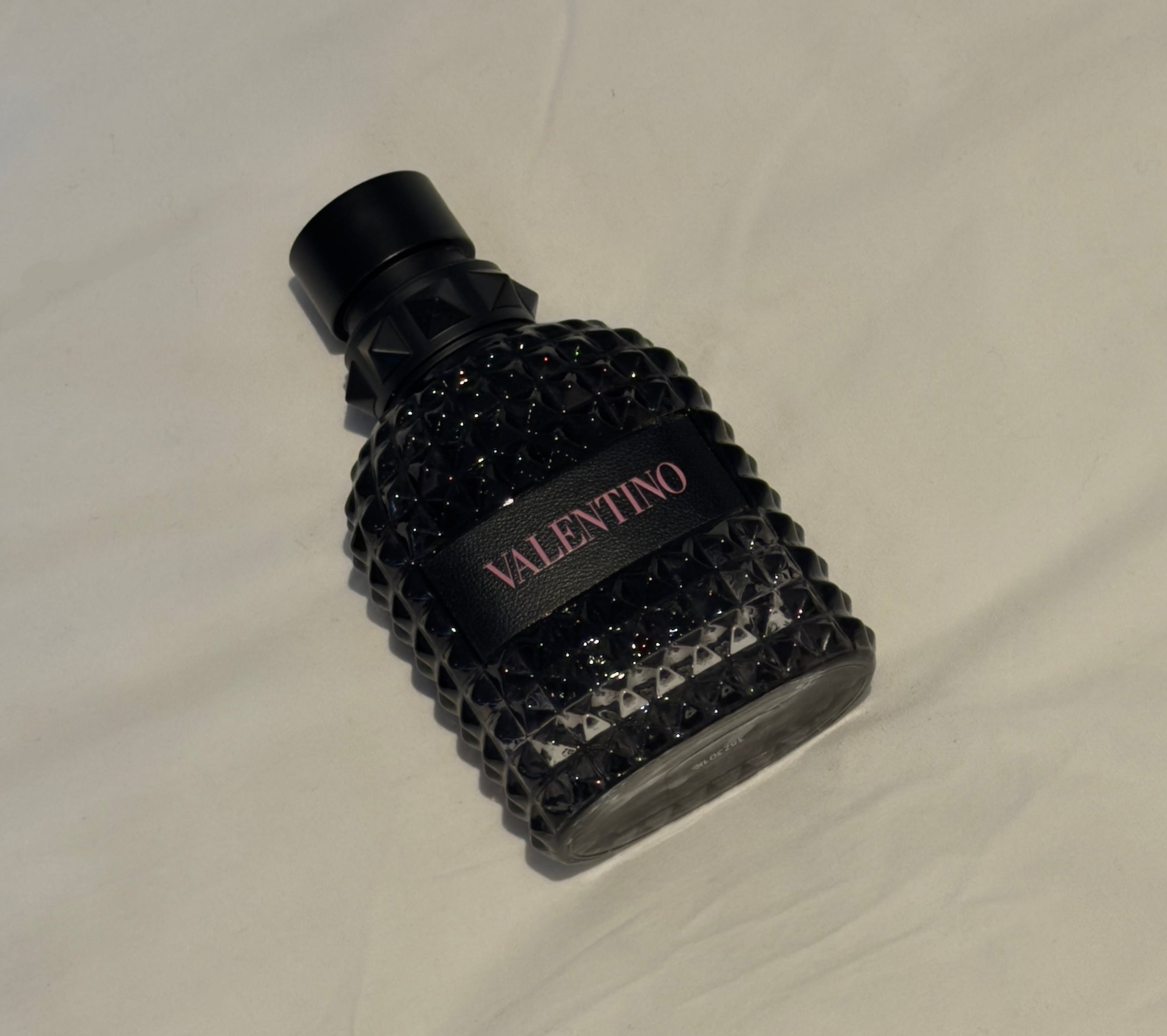 Black textured Valentino perfume bottle on a beige fabric background